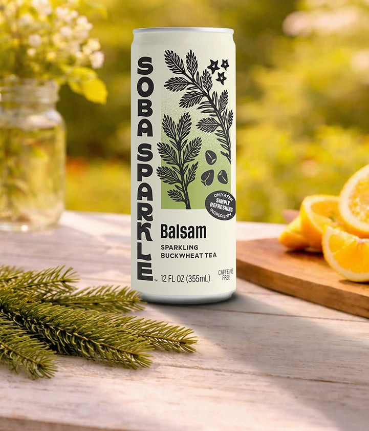 Sparklebuck Balsam sparkling buckwheat tea can on a wooden surface with greenery and oranges in the background.